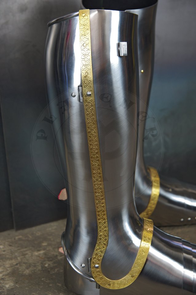 English style leg harness with fully closed cuisses, full greaves with characteristic line around outside ankles. Demi-greaves connected with greaves on rotary pin. Made of medium carbon steel of various thickness from 1 mm up to 1,5 mm. Heat hardened and tempered up to 42 HRC. Brass bands decoration motive based on example visible on Henry V tournament helm. Hand made steel buckles in set./Osony ng w stylu angielskim z w peni zamknitymi nabiodrkami, nagolennicami z charakterystyczn lini wok zewntrznej kostki. Demi-greave poczony z nagolennicami poprzez obrotowy pin. Wykonane ze stali redniowglowej rnej gruboci od 1 mm do 1,5 mm. Hartowane i odpuszczane do 42 HRC. Mosine listwy dekoracyjne z motywem wzorowanym na hemie turniejowym Henryka V. W zestawie rcznie robione sprzczki stalowe.